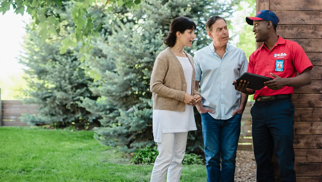 Two customers standing outside of their home speaking with a Mr. Rooter professional.