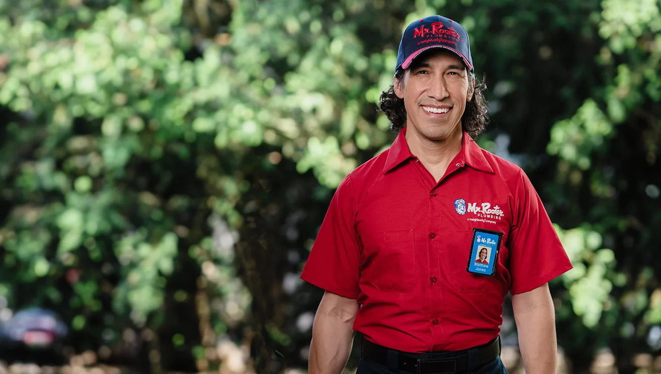 Mr. Rooter Plumbing professional standing outside with greenery in the background.