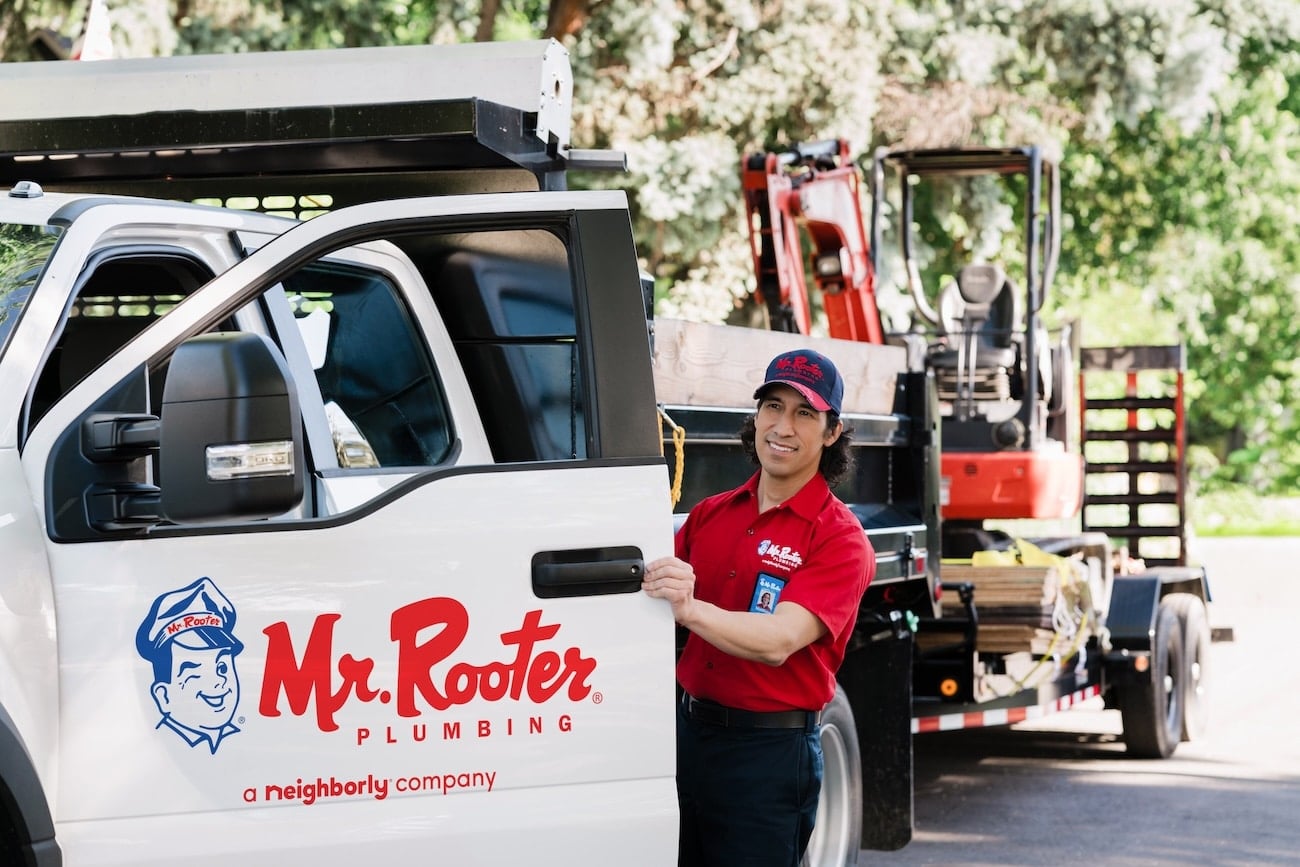 A Mr. Rooter employee outside a service truck loaded with equipment