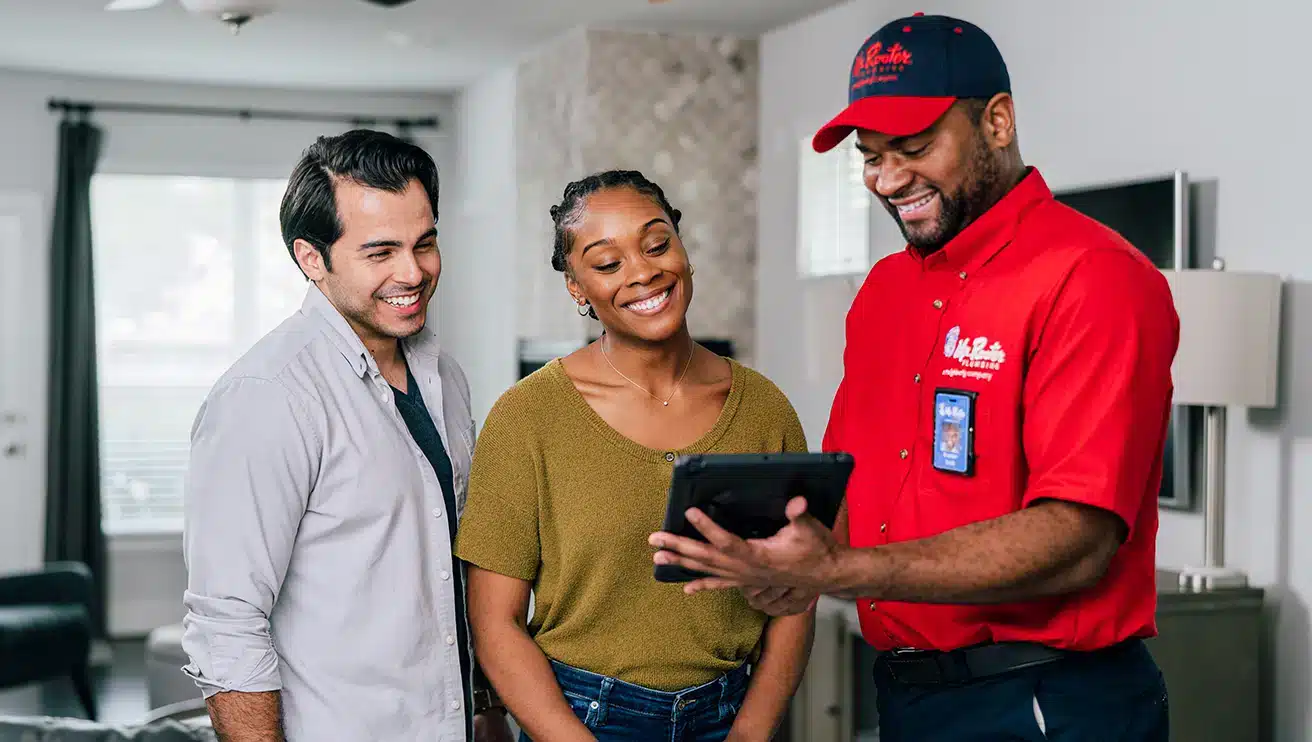 A uniformed Mr. Rooter professional discussing services with customers in their home