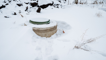 A septic tank is positioned right in the middle of a vast, snowcovered field, creating a striking contrast against the blanket of white that has gathered due to the winter season