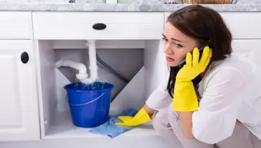 Sad woman calling plumber in front of leaky sink | Mr. Rooter Plumbing of Yavapai, Coconino & Maricopa Counties