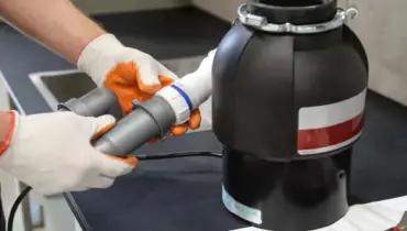 A close-up image of someone holding a sink&rsquo;s p-trap next to a garbage disposal sitting on the counter after it has been removed in order to complete garbage disposal repairs.